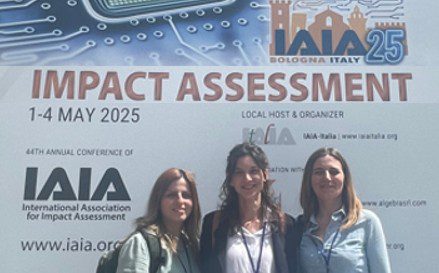 Three women standing in front of a banner for the IAIA 2025 Impact Assessment Conference held in Bologna, Italy from May 1–4, 2025.